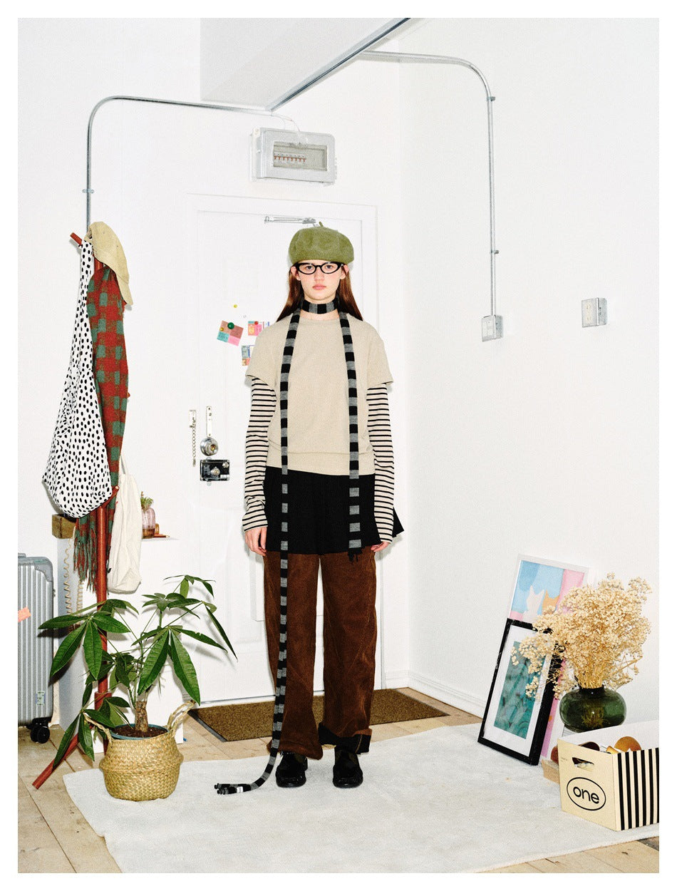 Front view of a model wearing a beige short-sleeve top over black-and-cream striped sleeves, a black skirt and brown