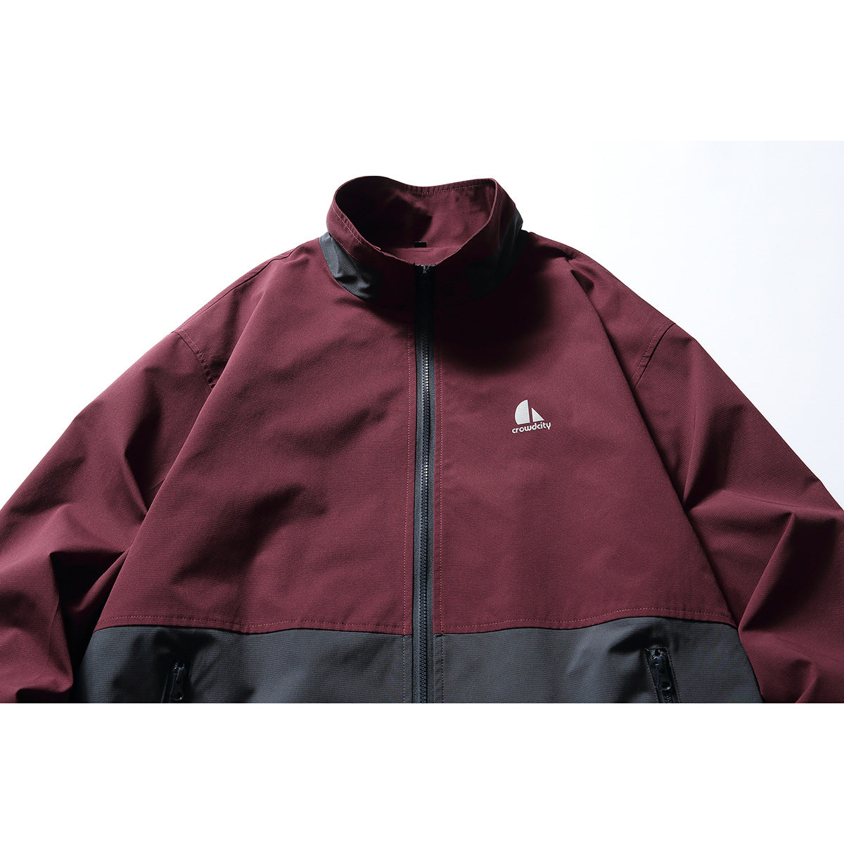 Close-up of a burgundy and charcoal color-block zip jacket with a stand collar and small chest logo.