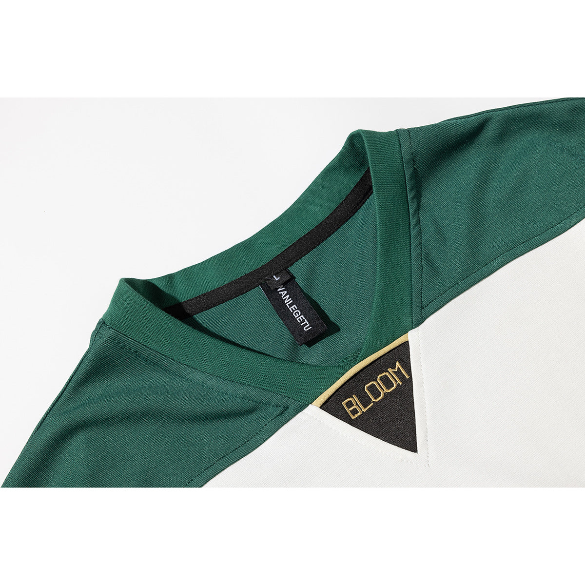 Close-up of a dark green shirt's V-neck, inner label, white chest panel, and small embroidered chest emblem.