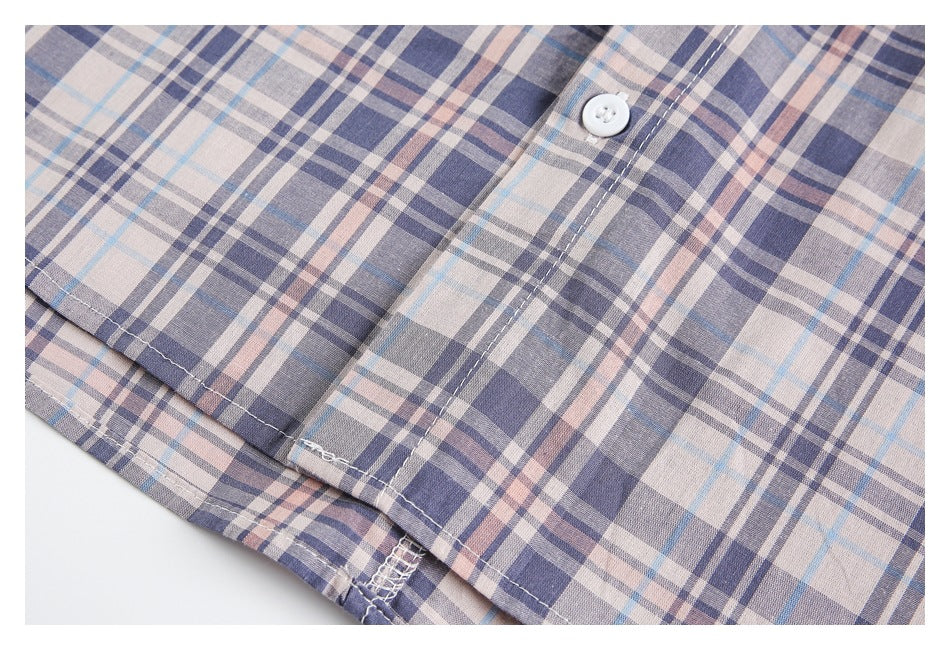 Close-up of the pale plaid shirt's button placket, hem, and stitched seams.