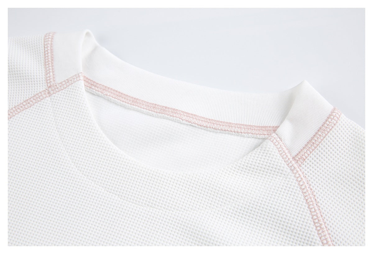 Close-up of a white shirt's ribbed crew neckline and pale pink raglan seam stitching.