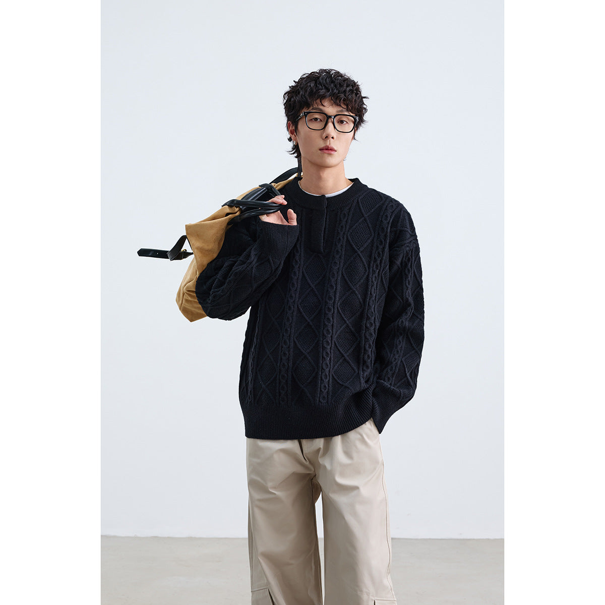 Model wearing a black cable-knit sweater with raised diamond patterns, ribbed trim, and a short front placket.
