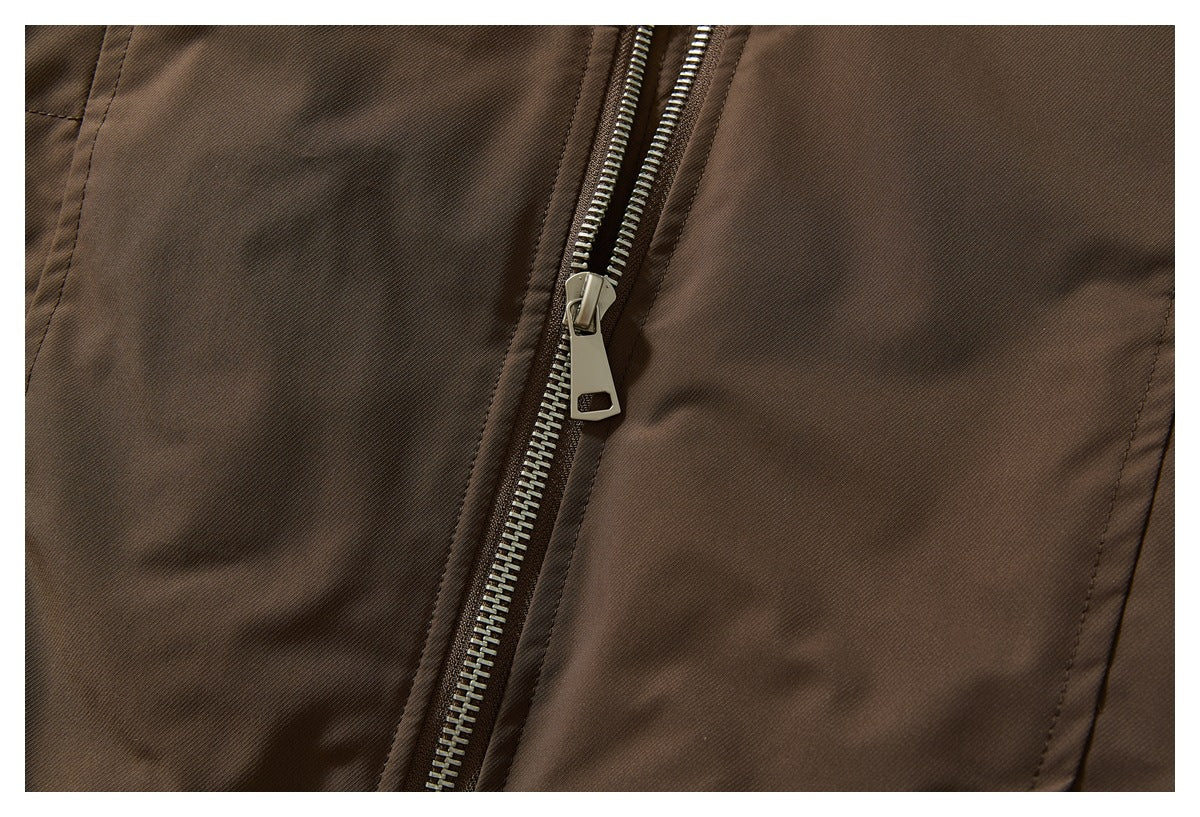 Close-up of the brown jacket's silver front zipper and pull against the smooth outer fabric.