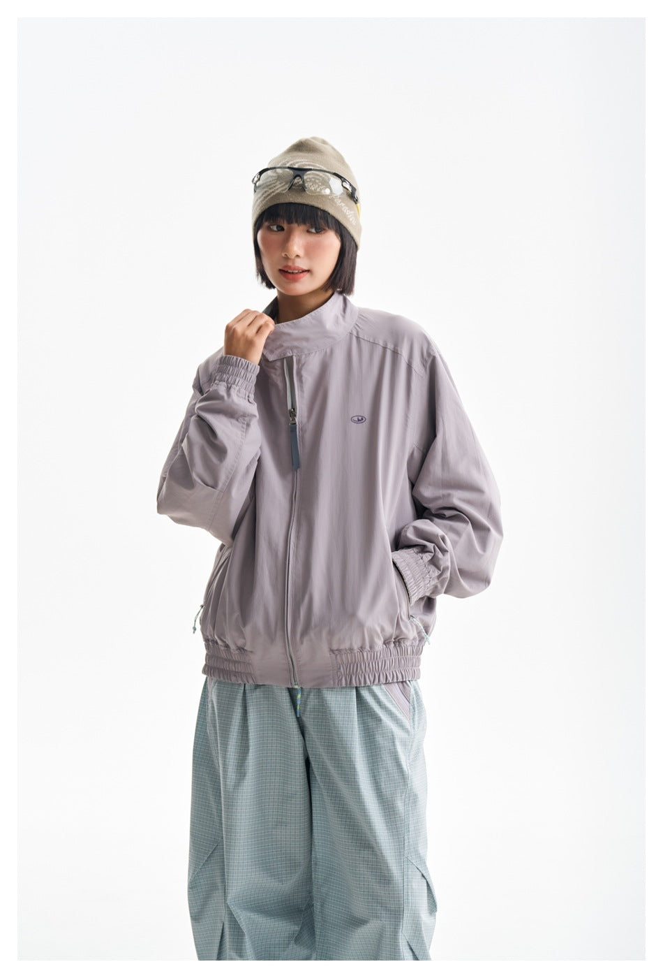 Closer front view of a model wearing a lavender-gray zip jacket with elastic cuffs and hem.
