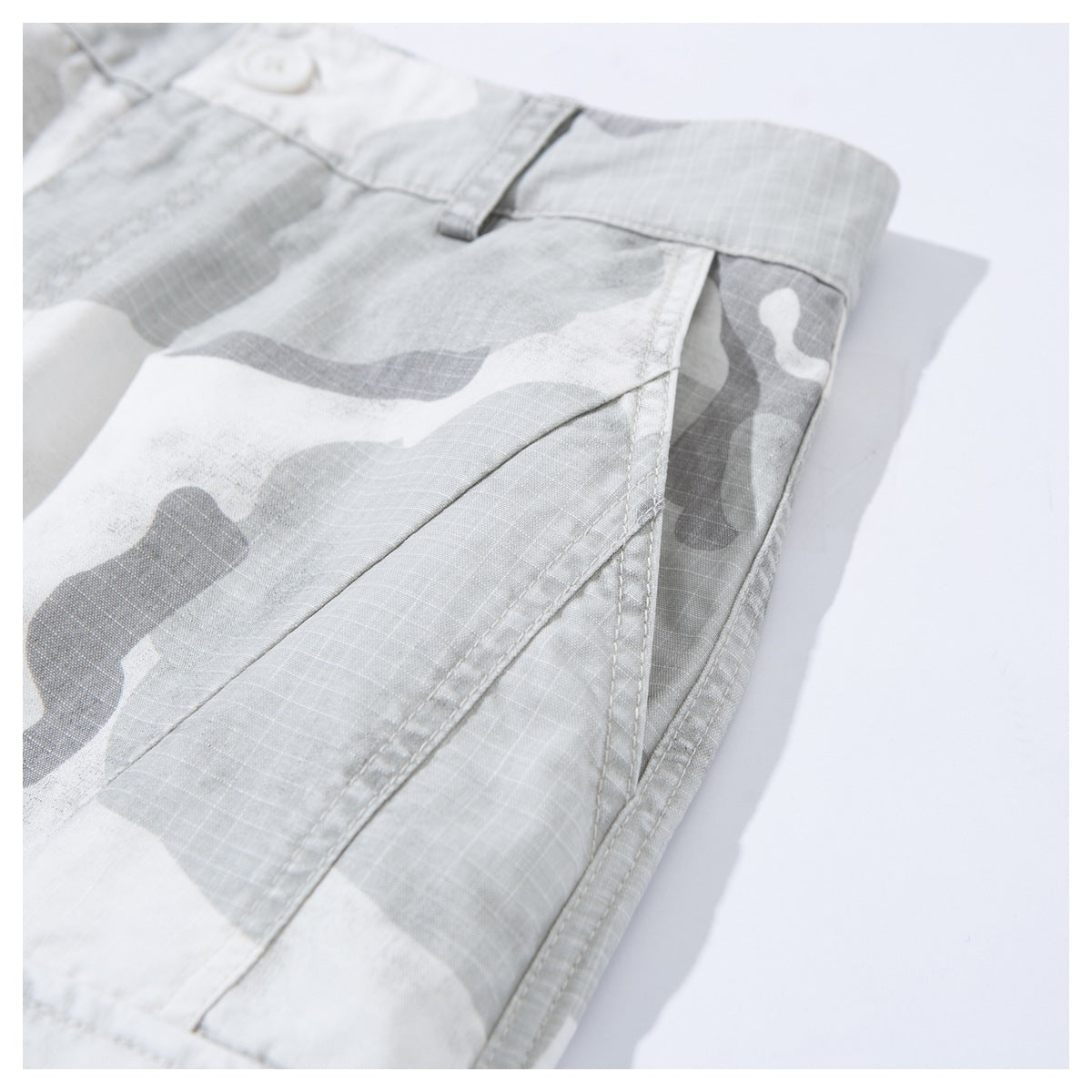 Close-up of light gray and white camouflage shorts showing the waistband, belt loop, and stitched side seam.