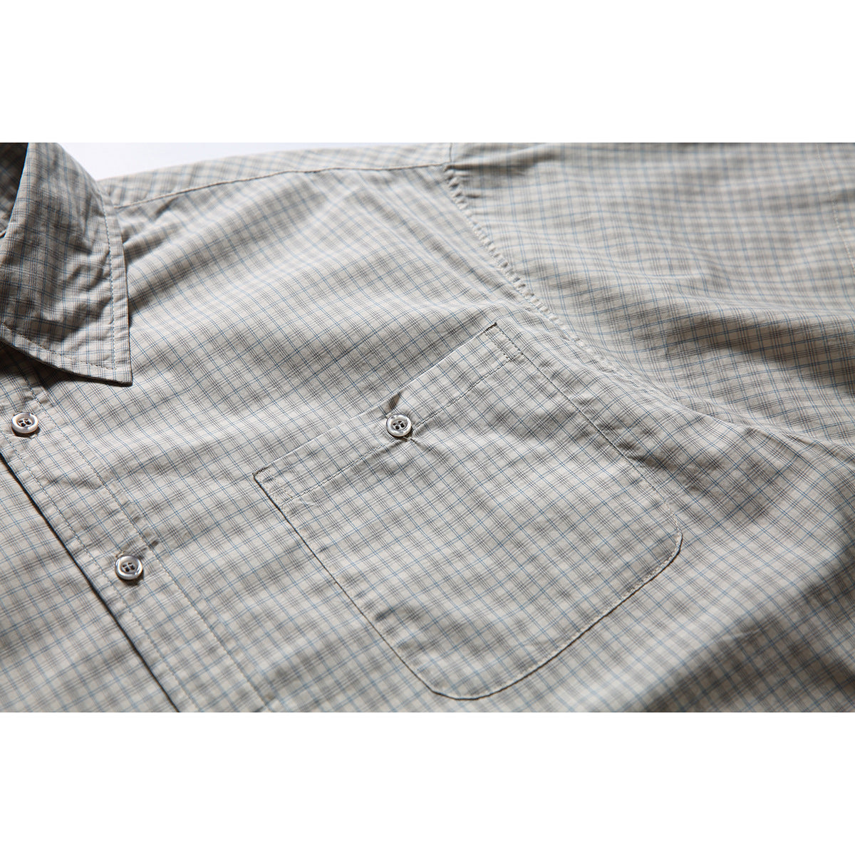 Close-up of the light gray plaid shirt’s buttoned chest pocket, front buttons, and short sleeve.
