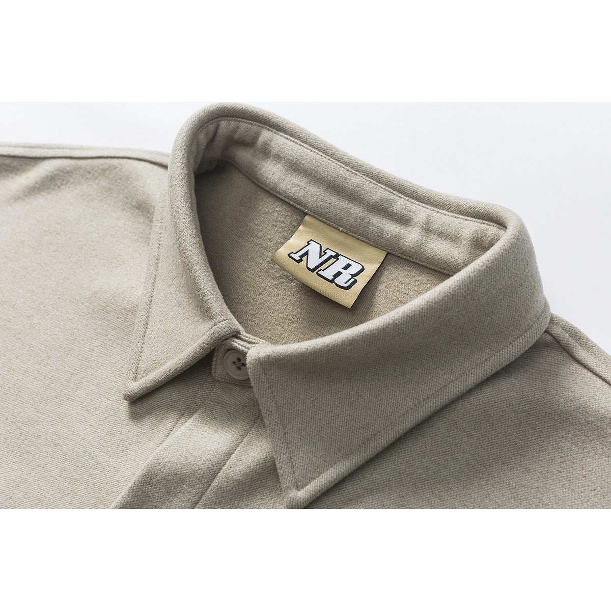 Close-up of a beige-gray shirt jacket’s wide collar, button, and sewn NB neck label.