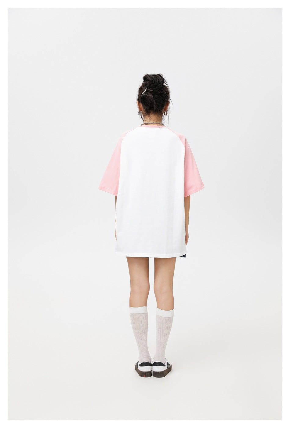 Back view of a model wearing a white raglan T-shirt with pink sleeves, plain back, denim skirt and white socks