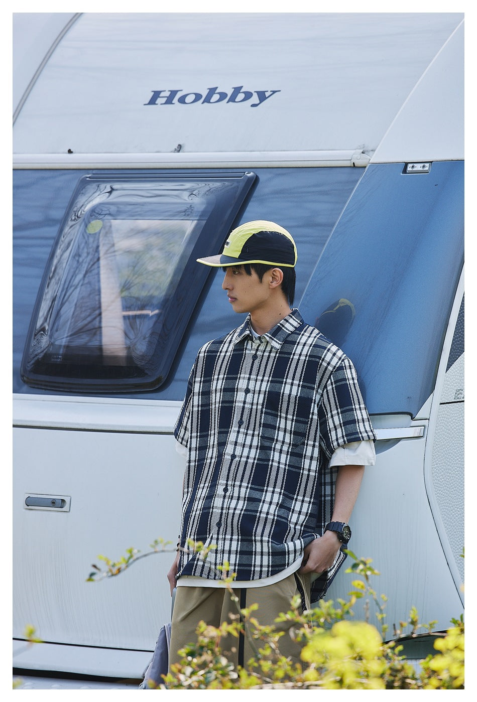 Model wearing a navy and white plaid short-sleeve button-up shirt outdoors.