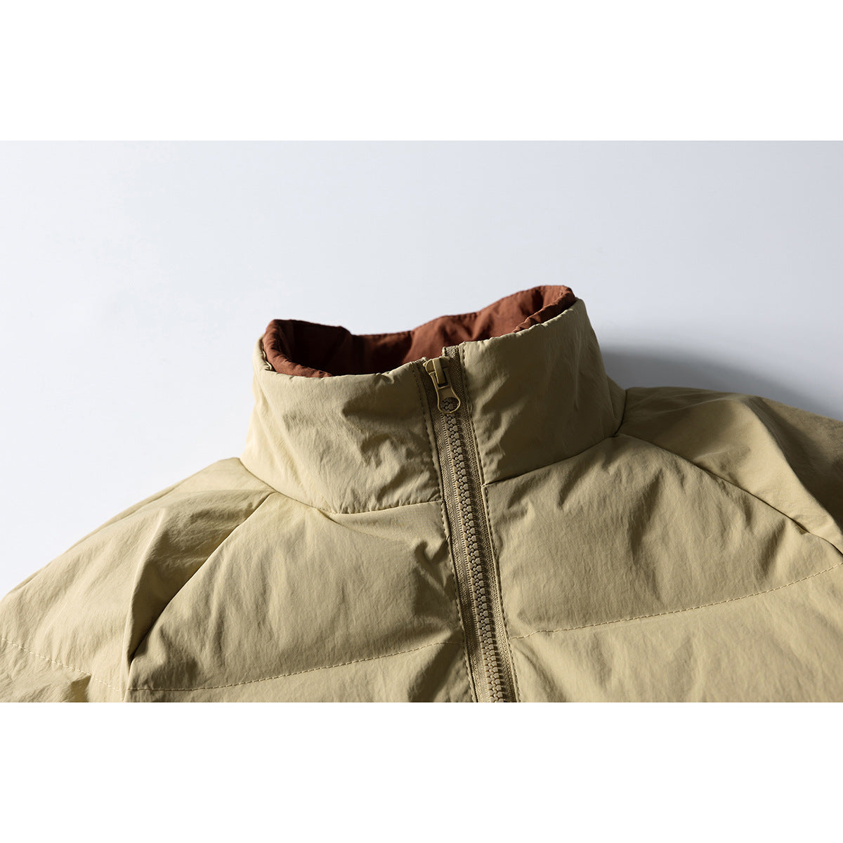 Close-up of a beige jacket's high collar, brown lining, and front zipper.