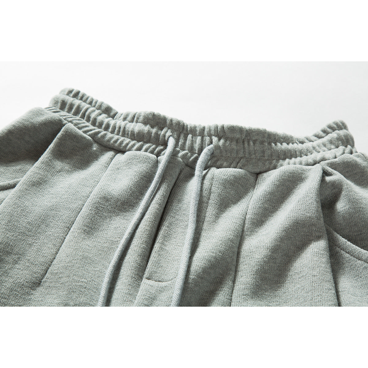 Close-up of light gray sweatpants showing the gathered elastic waistband, matching drawstrings and front pleats.