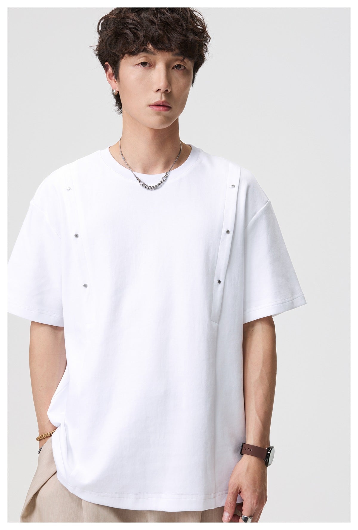 Close front view of a model in a white oversized tee with snap-fastened vertical straps across the chest.