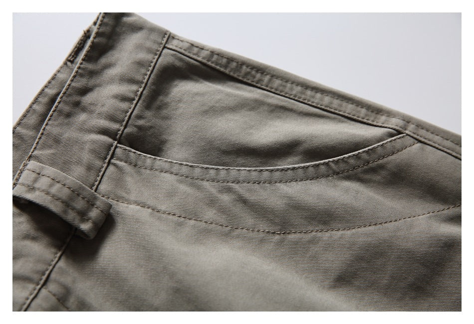 Close-up of a curved front pocket and belt loop on gray-olive pants.