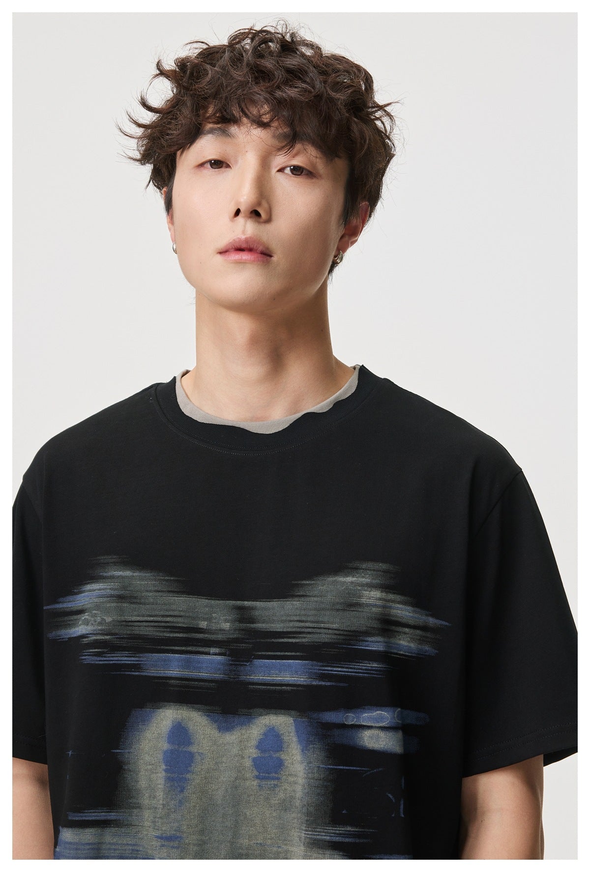 Close view of a model wearing a black T-shirt with an abstract blue and gray chest graphic and a contrasting gray inner