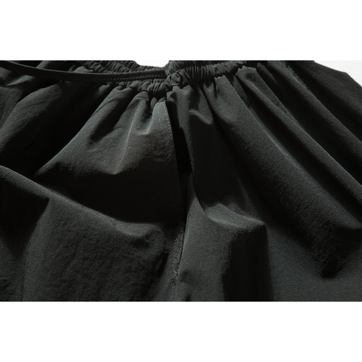 Close-up of black garment waistband, drawstring, and stitched fabric panels.