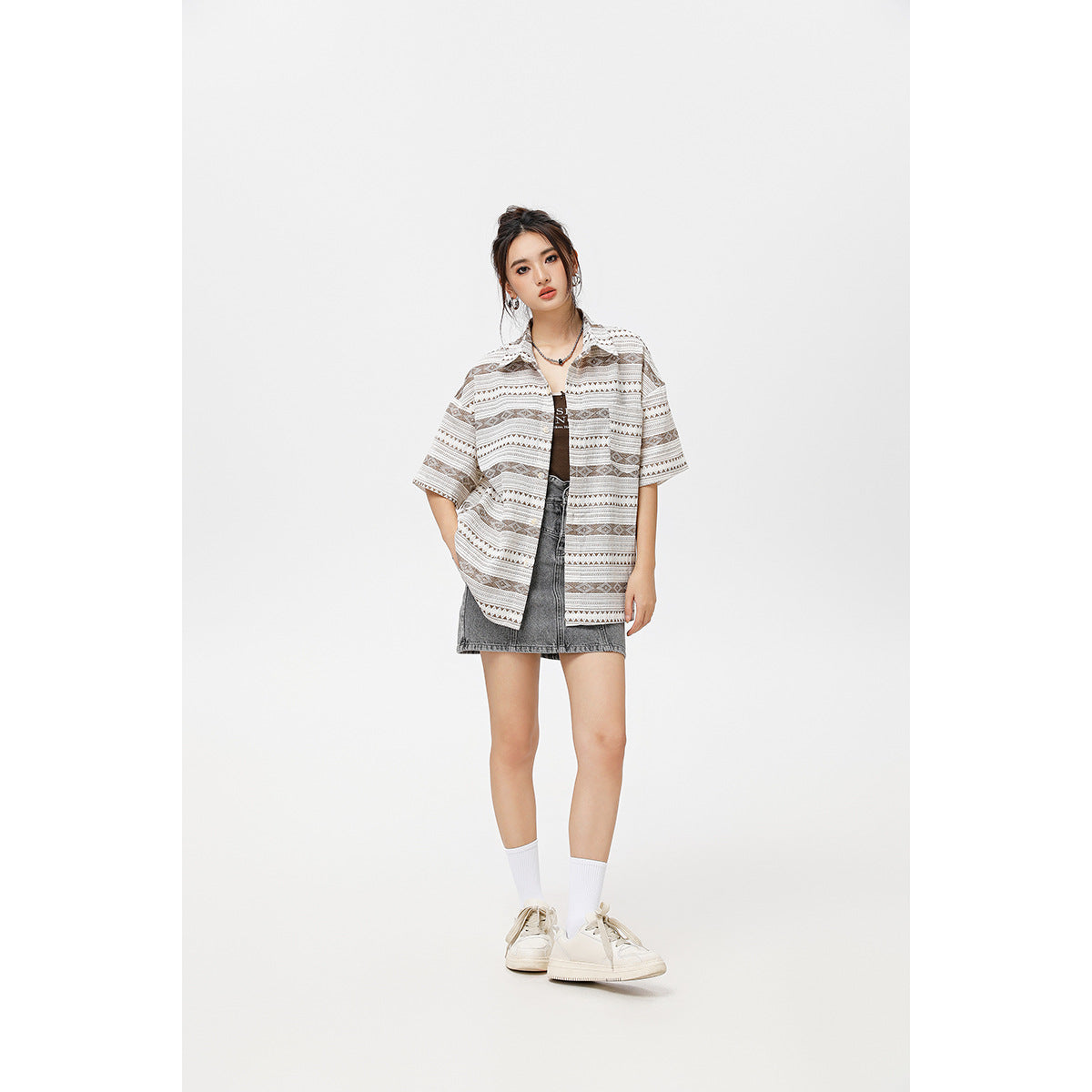 Model wearing a loose taupe geometric short-sleeve shirt over a black top and gray denim mini skirt.