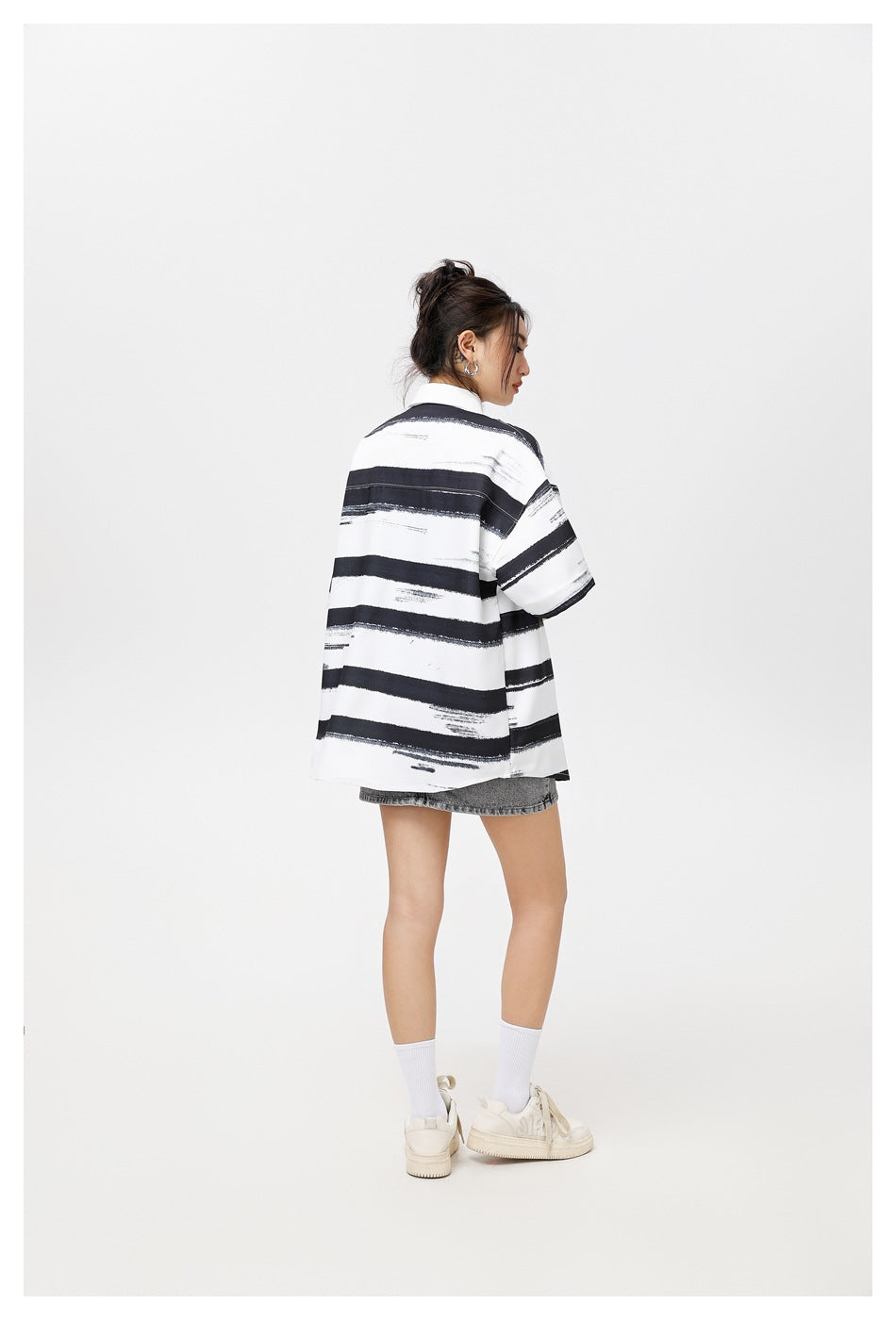 Back view of a model wearing an oversized black and white striped short-sleeve shirt with a gray denim skirt
