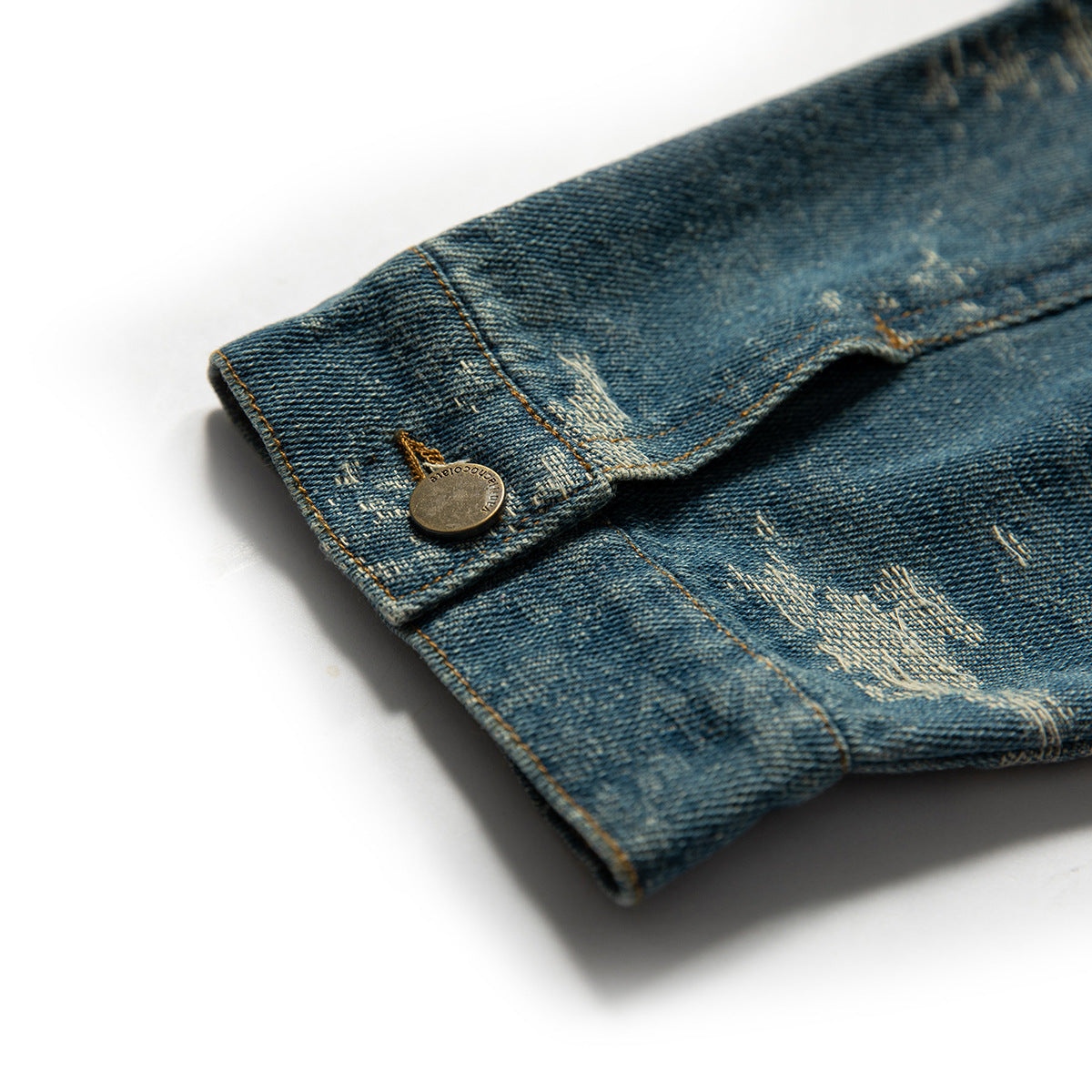 Close-up of a distressed blue denim sleeve cuff with a brass-tone button and contrast stitching.