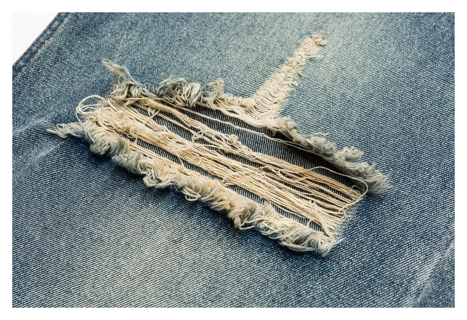 Close-up of a frayed horizontal rip in blue denim, exposing dark threads beneath the loose pale fibers.