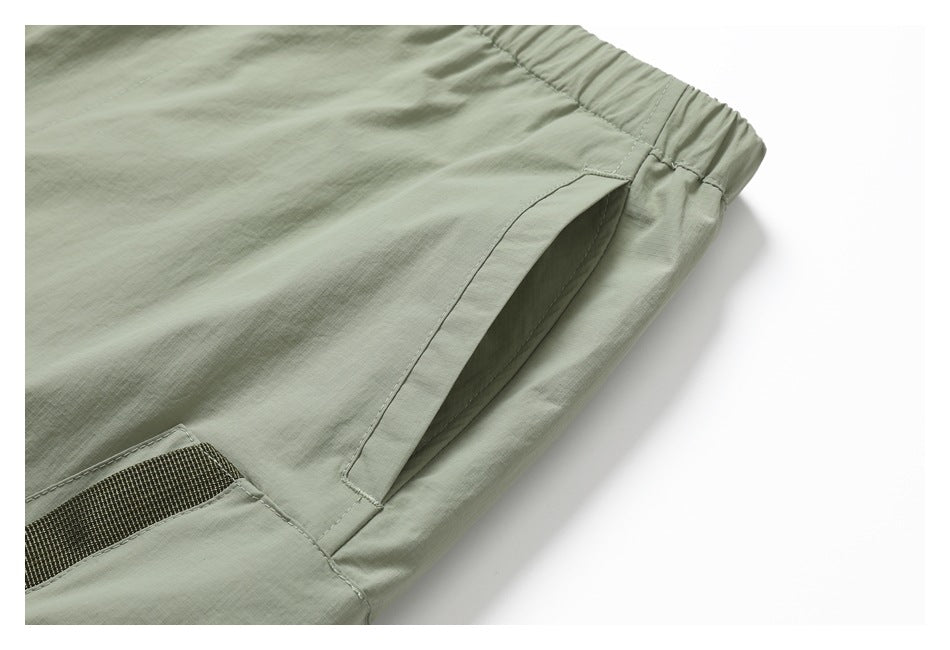 Close-up of sage pants showing a deep side pocket opening, elastic waistband, and part of a mesh-panel pocket.