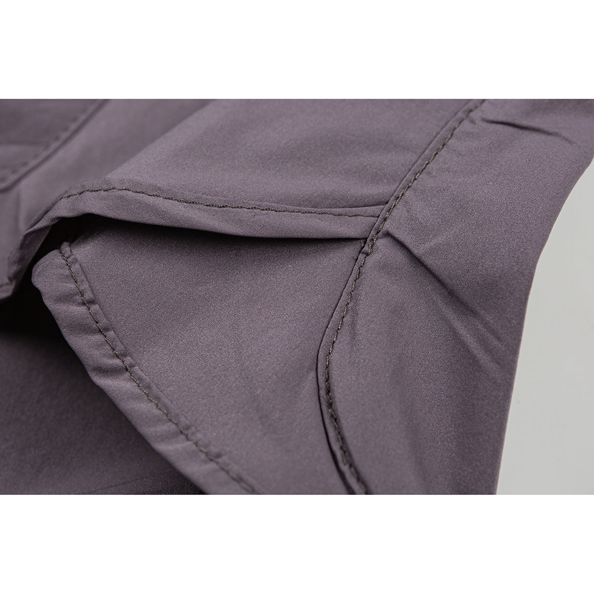 Close-up of mauve-gray shorts showing a curved seam and pocket opening.
