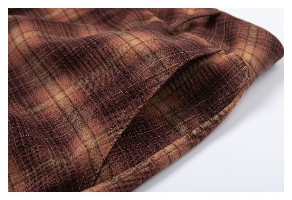 Close-up of a curved pocket opening and stitching on brown and tan plaid trousers.