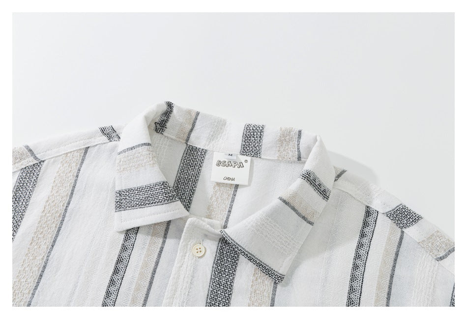 Close-up of a white collared shirt with black and beige woven stripes, a button, and a sewn-in neck label.