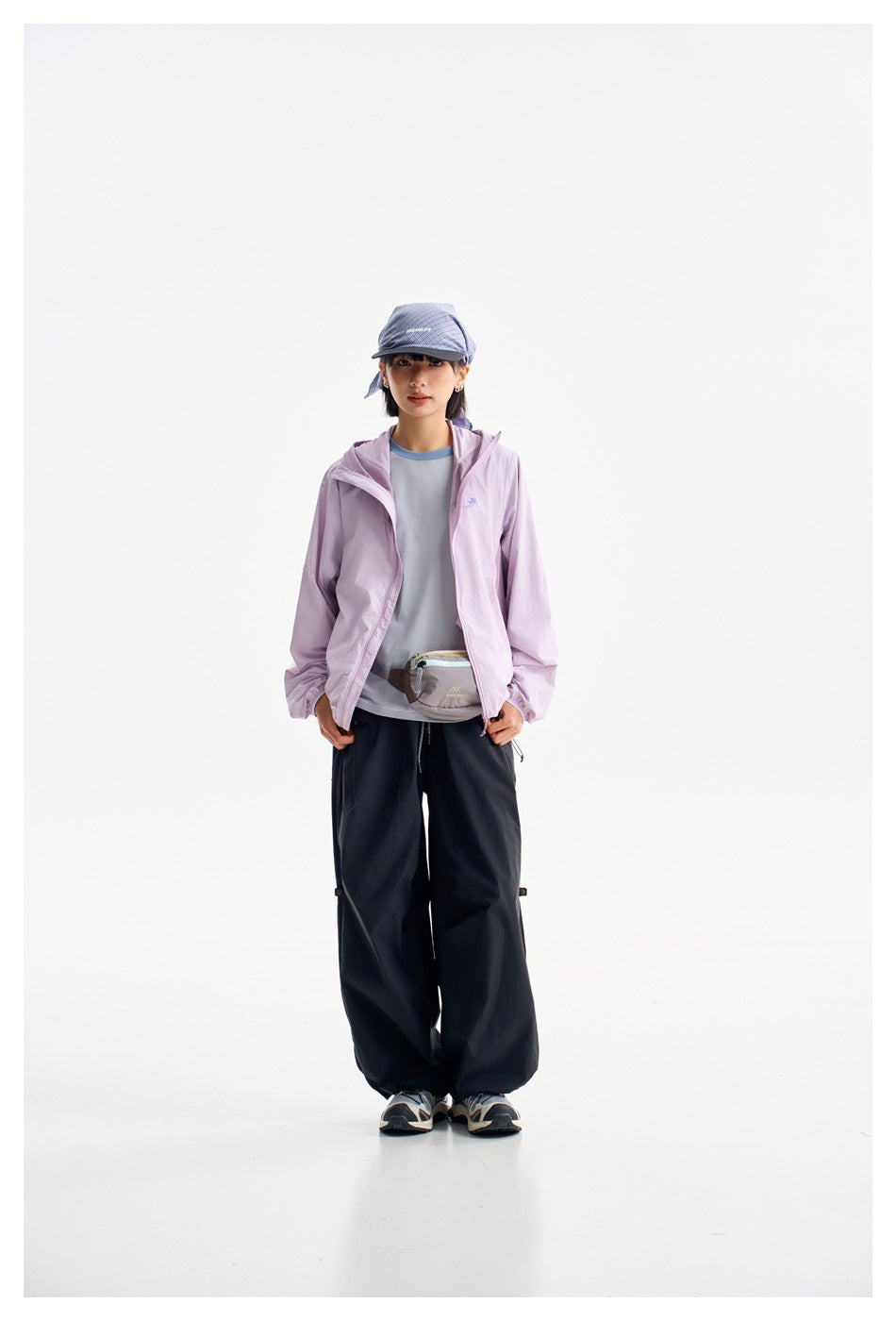 Full-length model wearing a lavender hooded jacket, dark trousers, and a cap against a white background.
