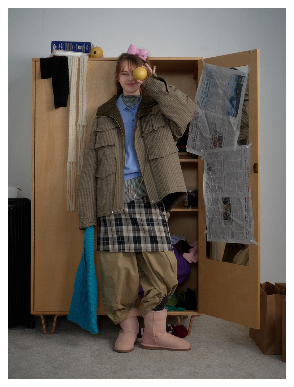 Model wearing the green checked pocket jacket open over a blue polo and plaid skirt, holding a lemon in front of a wardrobe