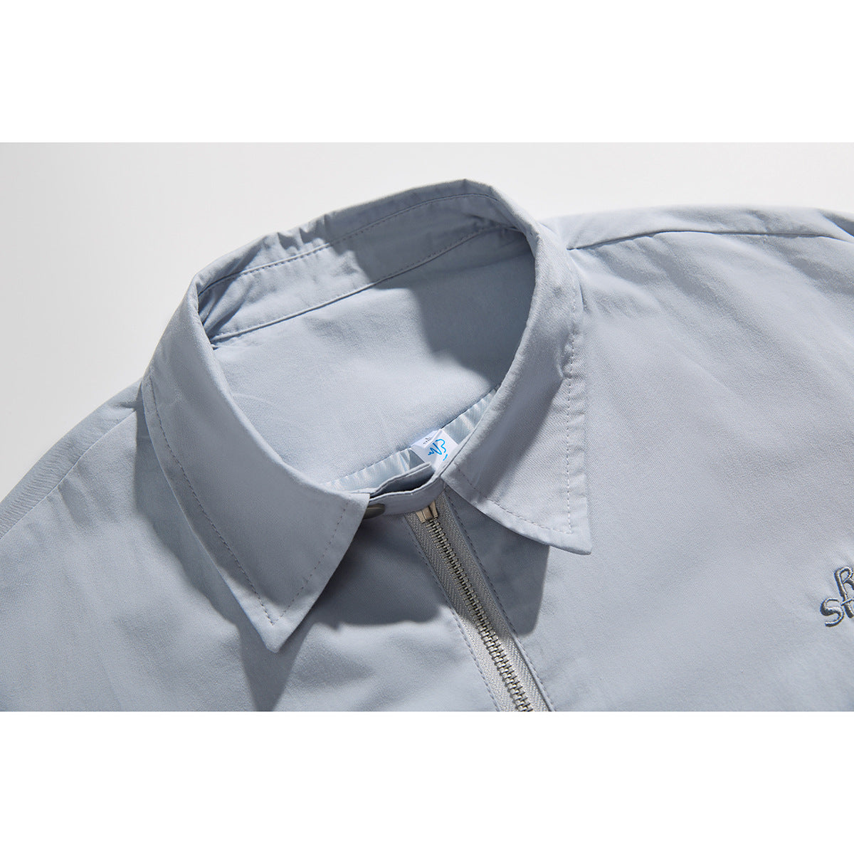 Close-up of a light blue-gray jacket collar, front zipper and partial chest embroidery.