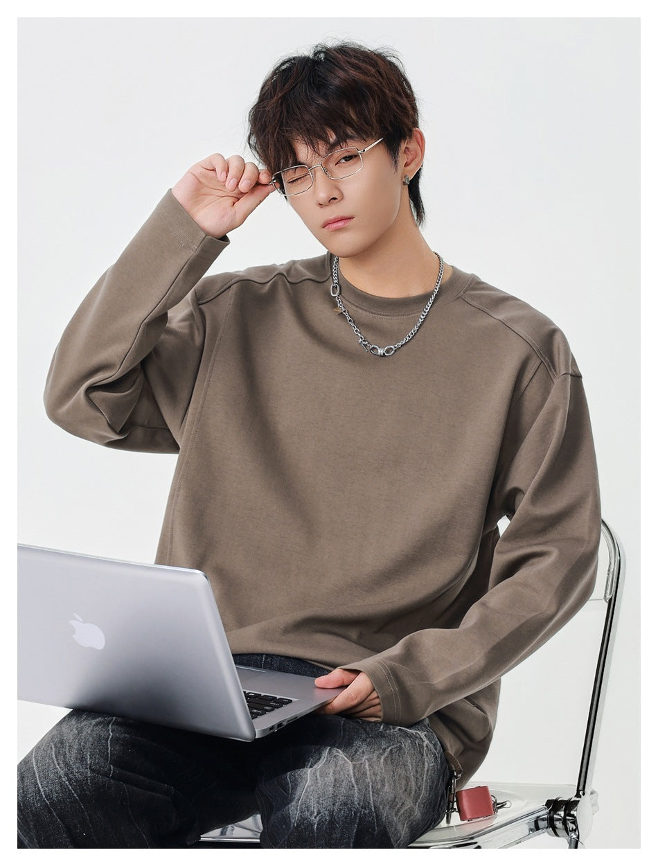 Man in a brown long-sleeve crewneck top sitting with a laptop and adjusting his glasses
