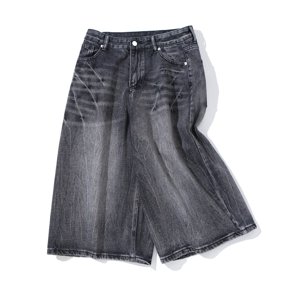 Washed black gray wide-leg denim shorts laid at an angle showing faded wash and front zip closure