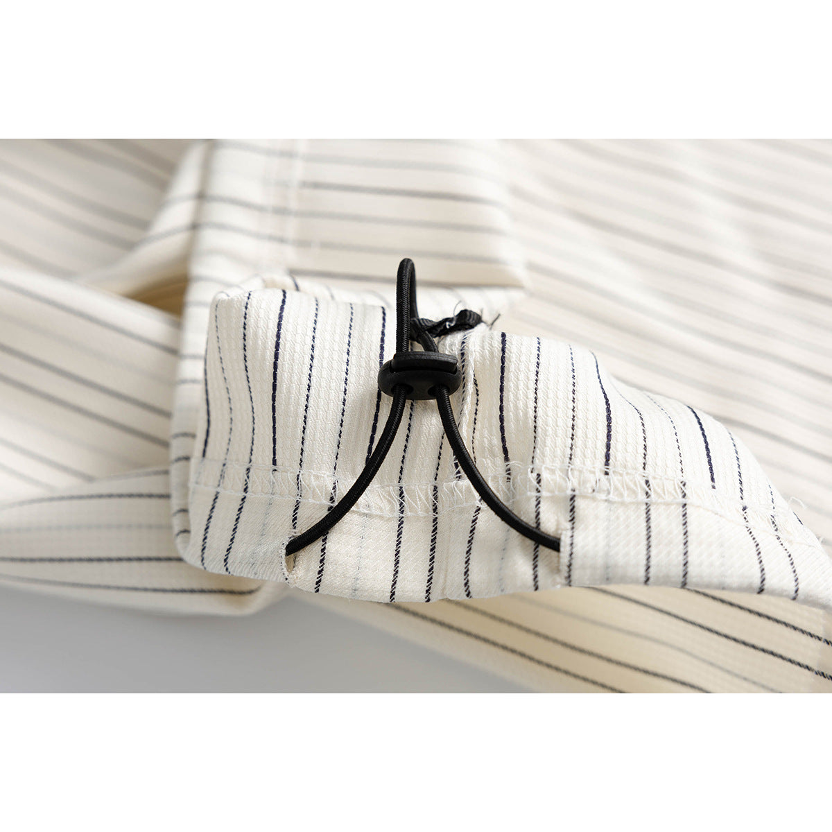 Close-up of a cream pinstriped sleeve cuff with a black elastic drawcord and toggle.