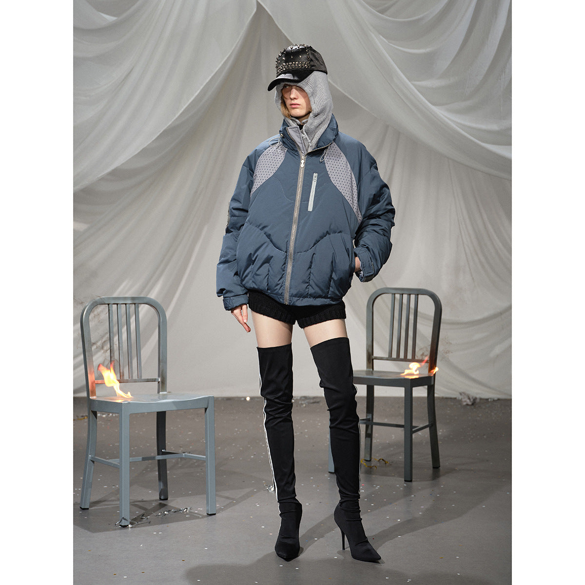 Model wearing a blue-gray padded jacket with dotted gray shoulder panels, a high collar and zip pockets.