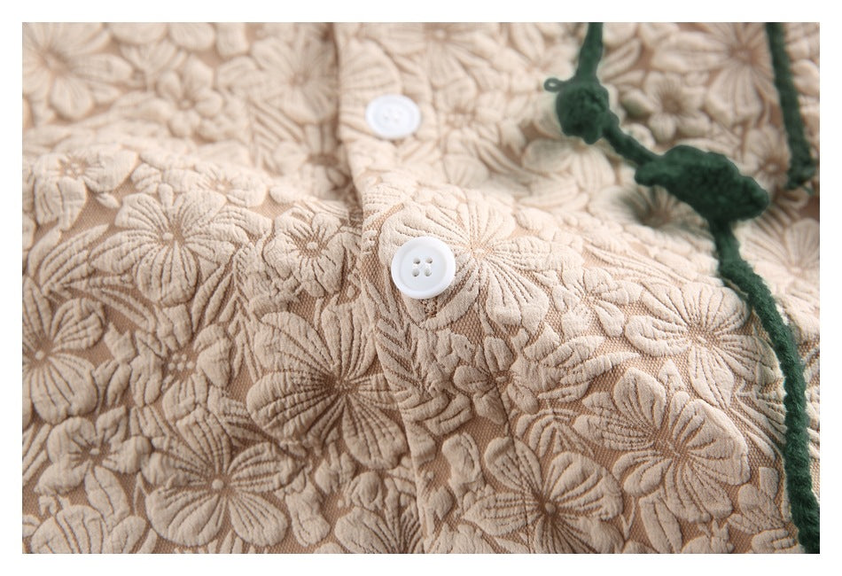 Close-up of a white button and raised floral texture on the beige garment, with a green cord at the edge.