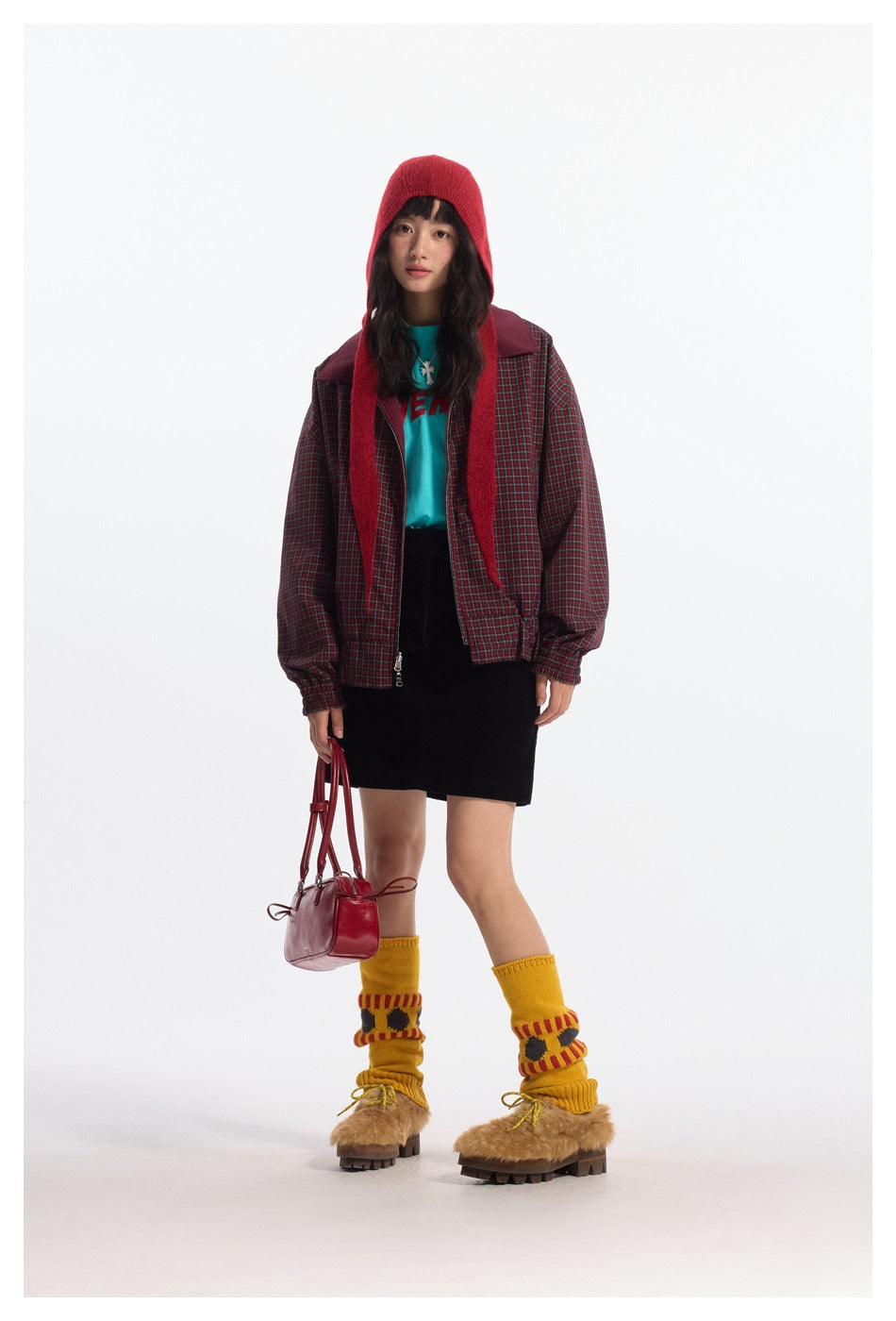 Full-length front view of a model wearing a red-and-green plaid jacket with burgundy shoulder panels and a red knit hood.