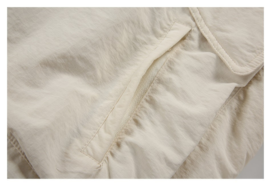 Close-up of a cream jacket's narrow zippered pocket and stitched flap.