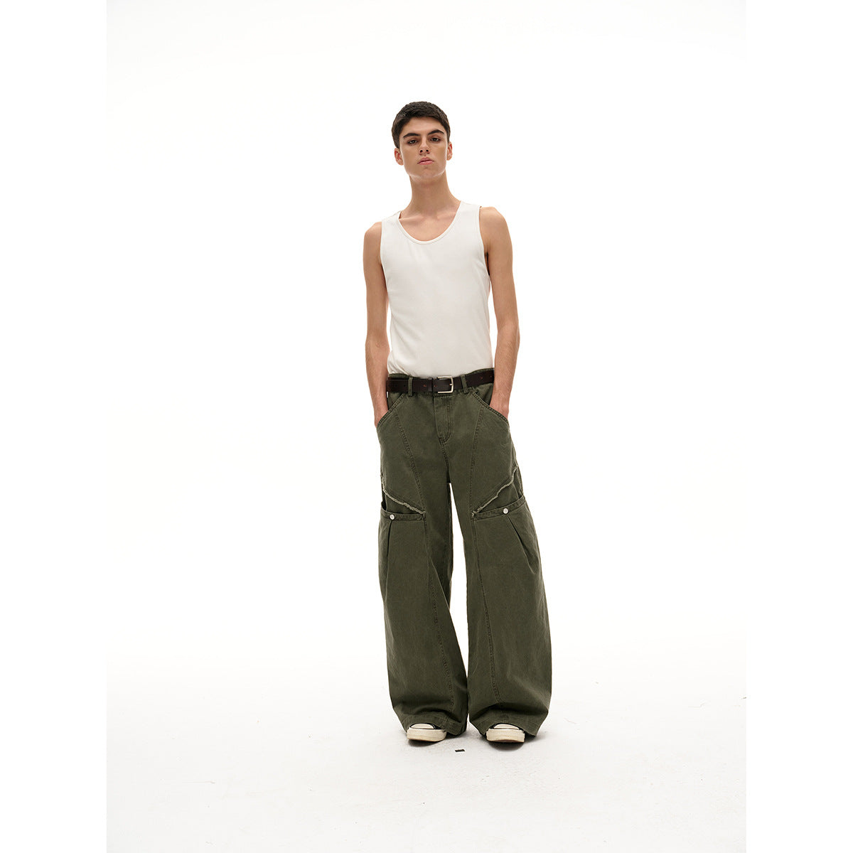Model facing forward in a white tank top and olive wide-leg pants with buttoned knee panels and a black belt.