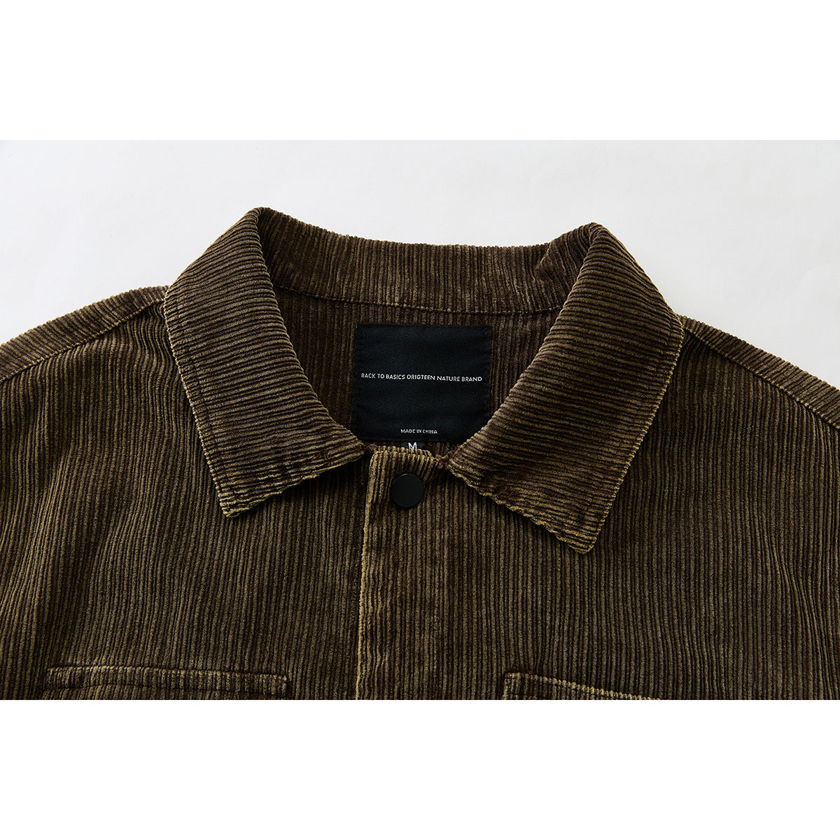 Close-up of a brown corduroy jacket collar, front snap, and black neck label.