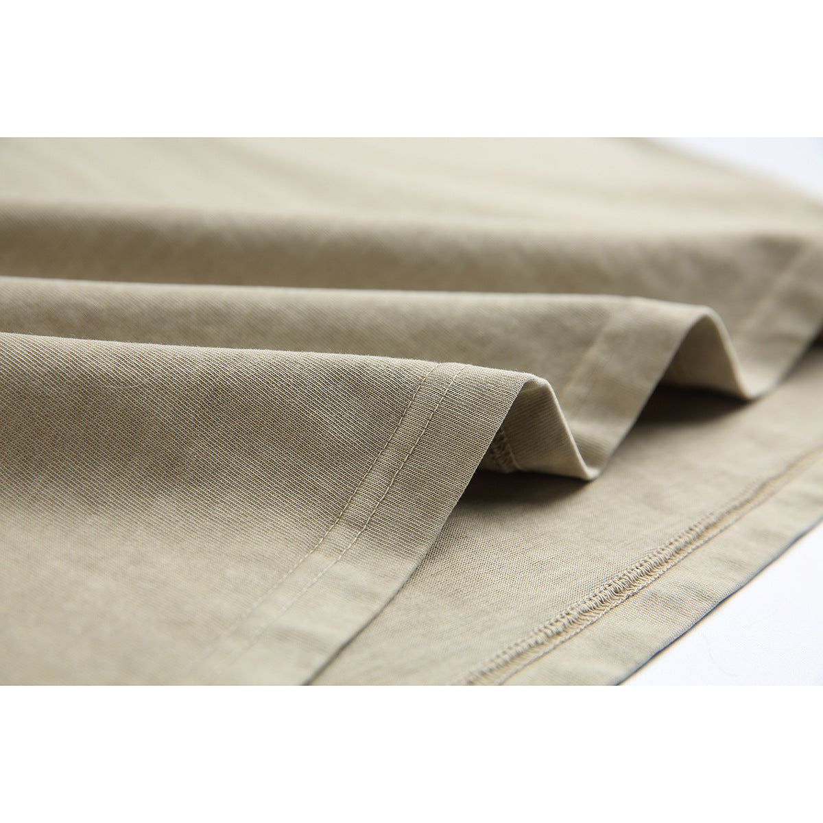 Close-up of the beige T-shirt’s folded fabric and double-stitched hem.