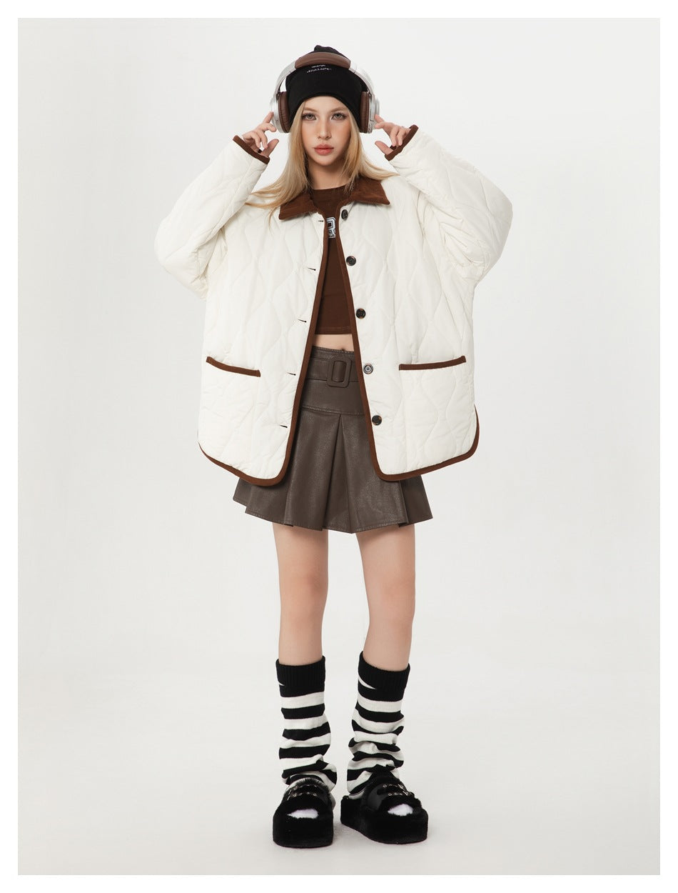 Model wearing oversized off-white quilted jacket with brown trim and patch pockets, front view with raised hands