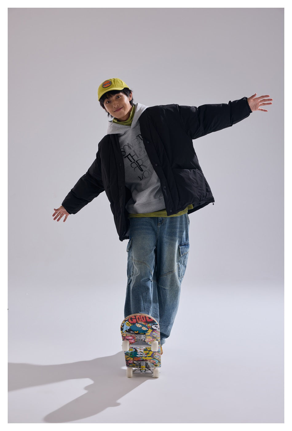 Model wearing an oversized black quilted jacket with snap closures, posed with arms out above a skateboard.