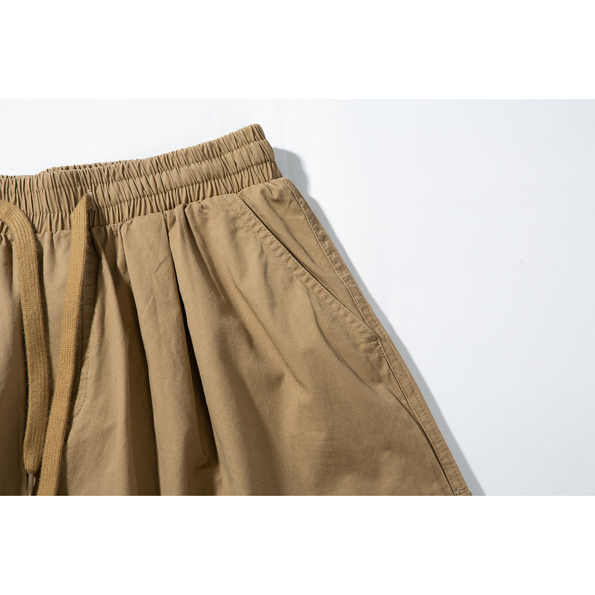 Close-up of tan shorts showing the elastic waistband, drawstring and slanted side pocket.