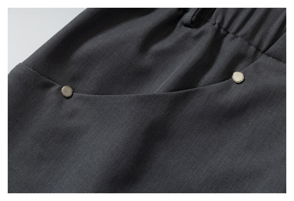 Close-up of a charcoal trouser pocket with two small metal studs and part of the elastic waistband.
