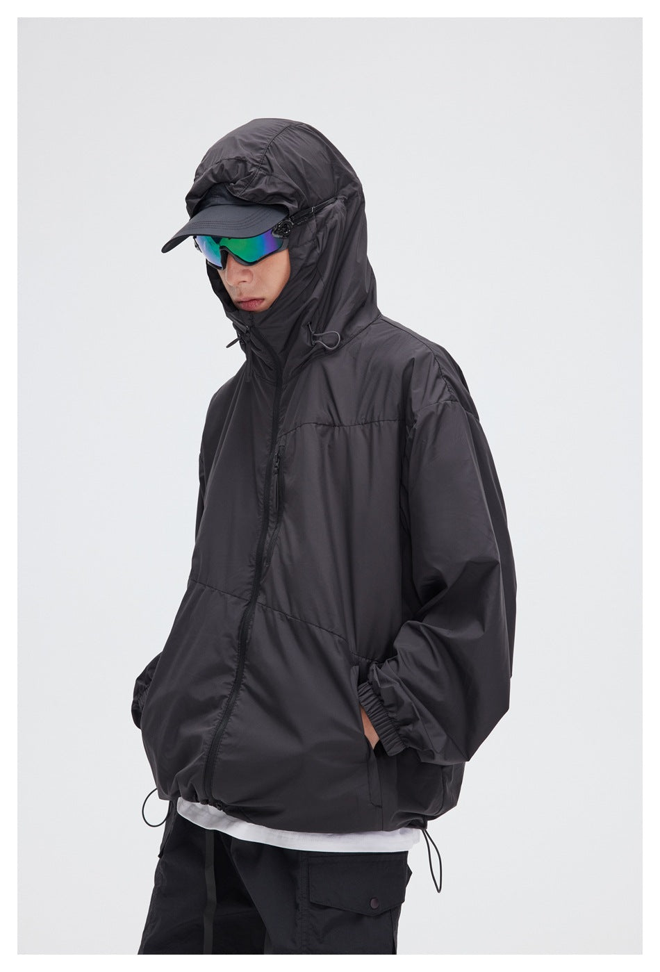 Close view of a model wearing a charcoal hooded jacket with a cap and mirrored sunglasses.
