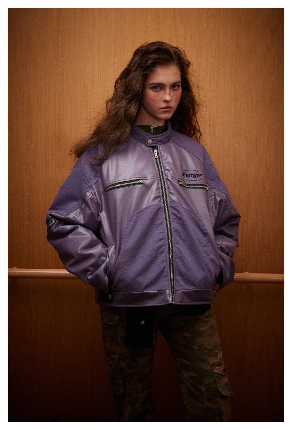 Front view of a model wearing a purple zip jacket with chest pockets and camouflage pants.