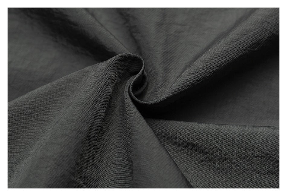 Close-up of charcoal gray fabric gathered into a soft spiral, showing its fine surface texture.