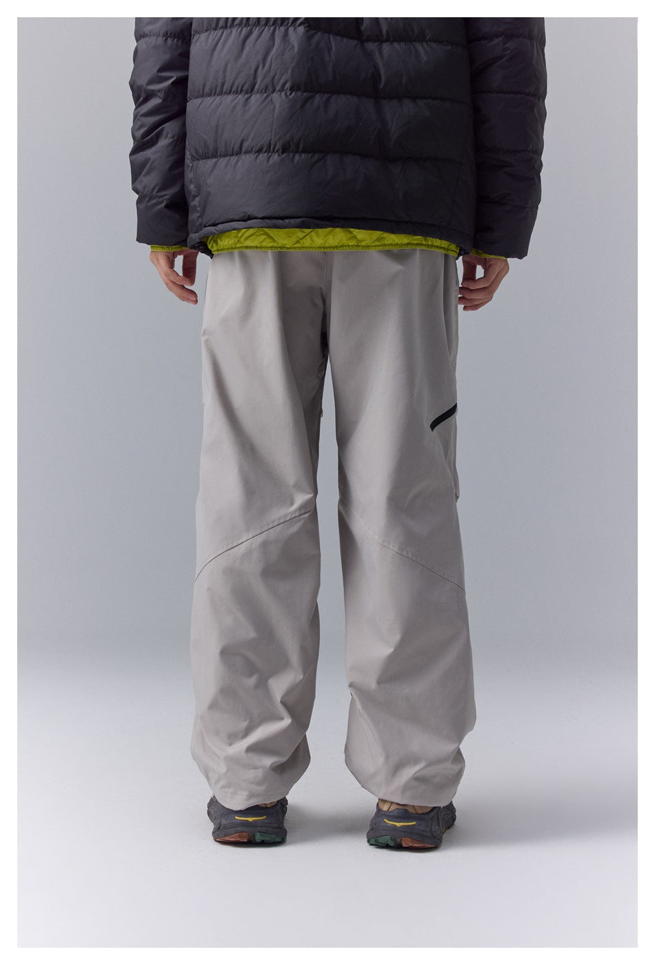 Back view of loose-fit light gray pants worn with a black jacket with lime-green lining.