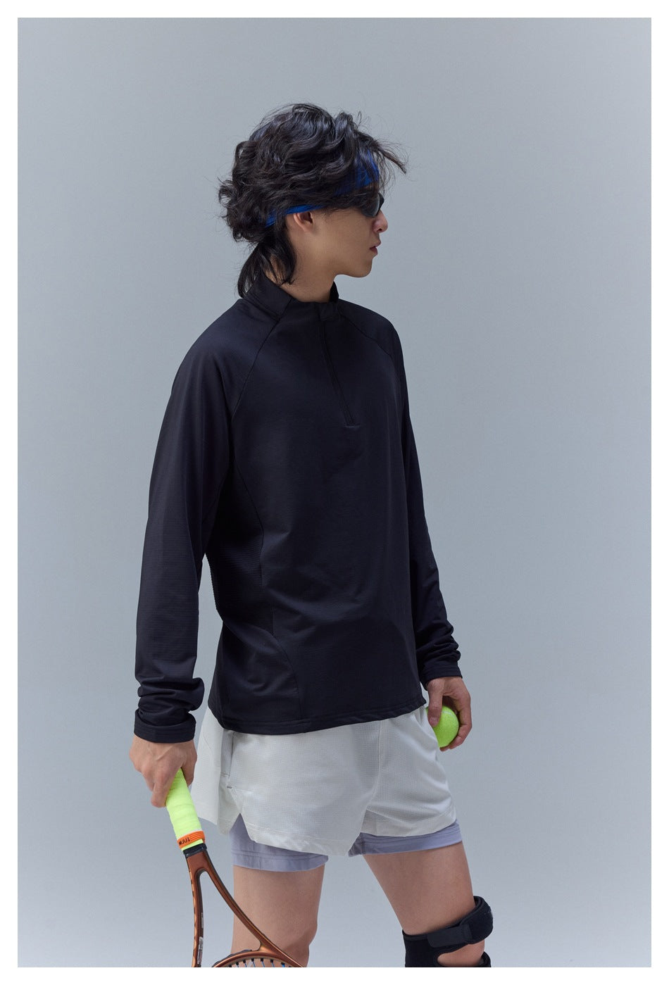 Side view of a model wearing a black long-sleeve quarter-zip top and light shorts with a lavender underlayer.