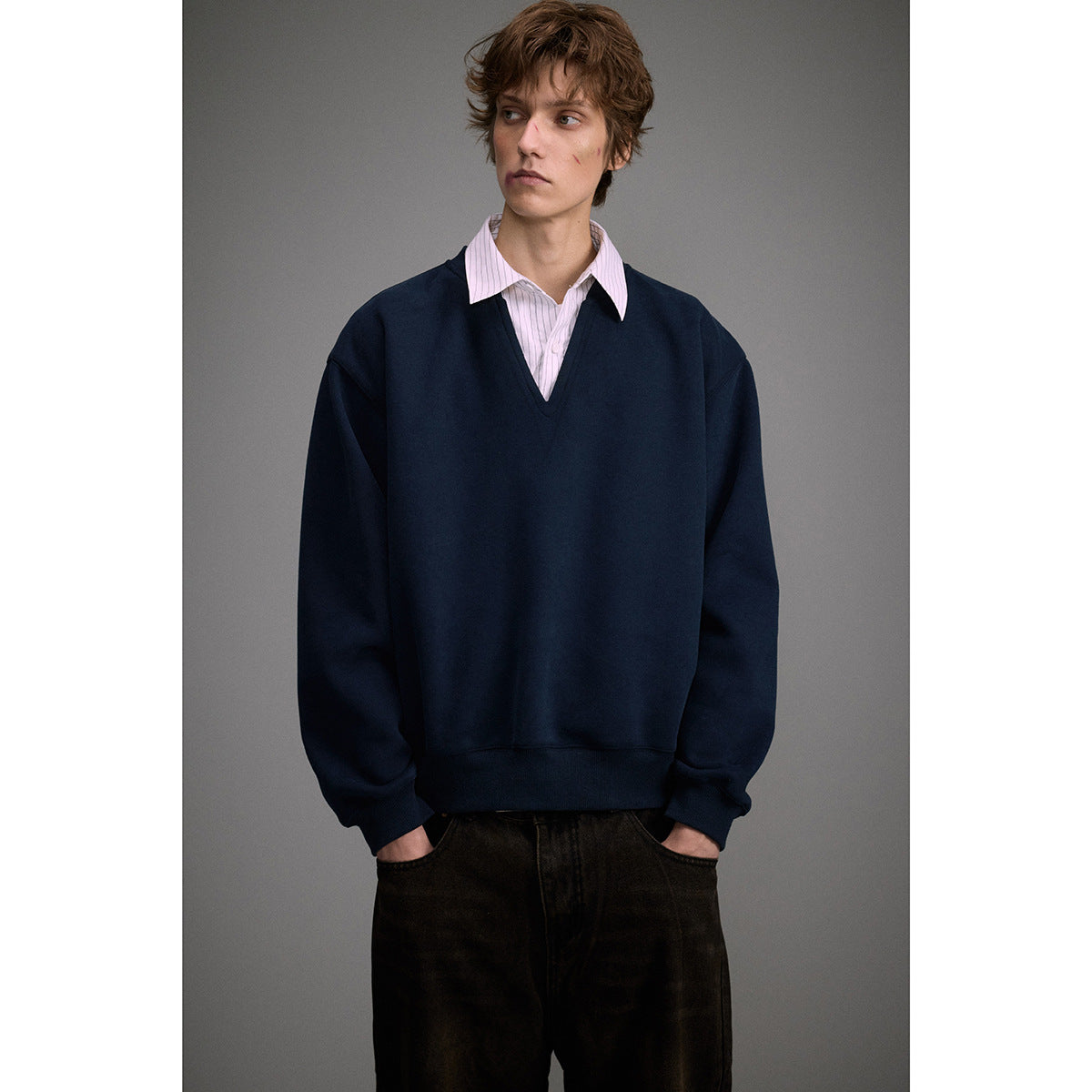 Waist-up view of a model in an oversized navy V-neck sweatshirt layered over a pale pink striped shirt.